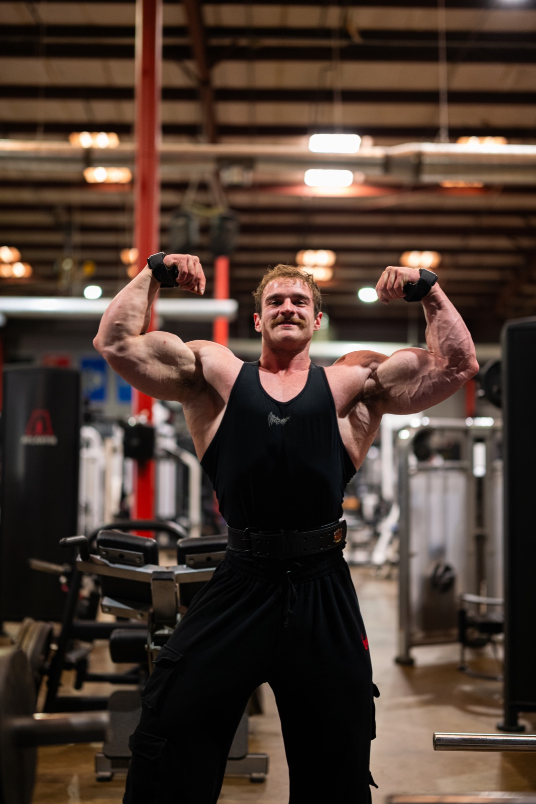 Physique athlete hitting a front double-biceps pose in the gym